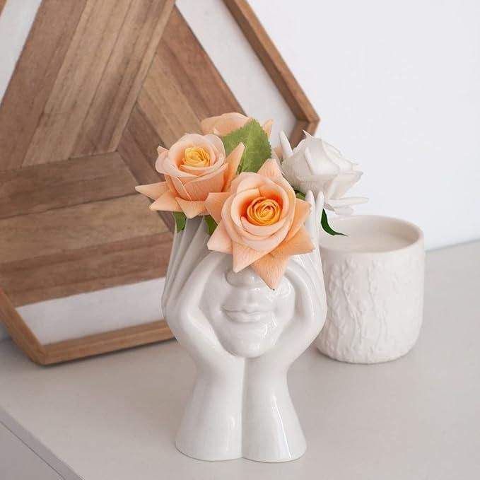 White vase shaped like a face with peach roses on a light surface.