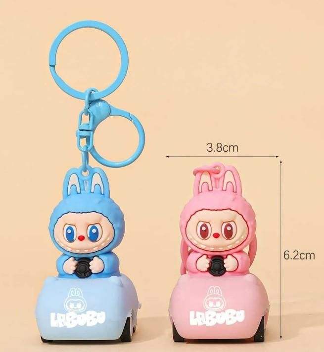Two cartoon character keychains, one blue and one pink, on a beige background with measurements indicated.
