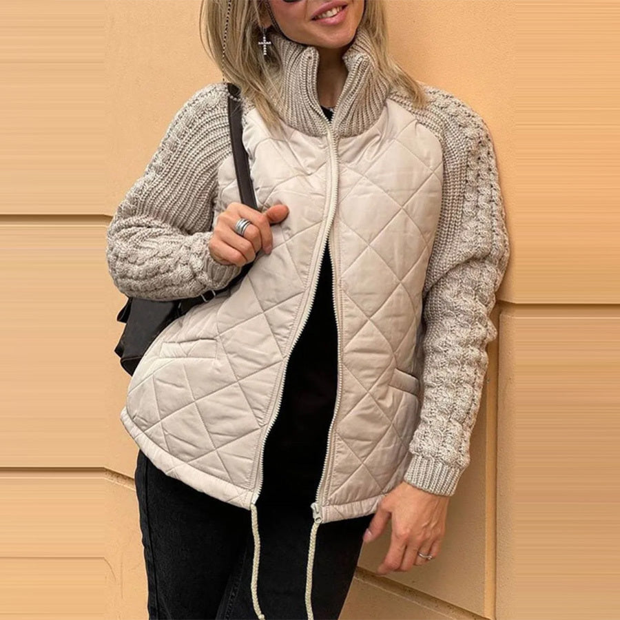 Person wearing a beige quilted jacket with knitted sleeves against a beige wall.