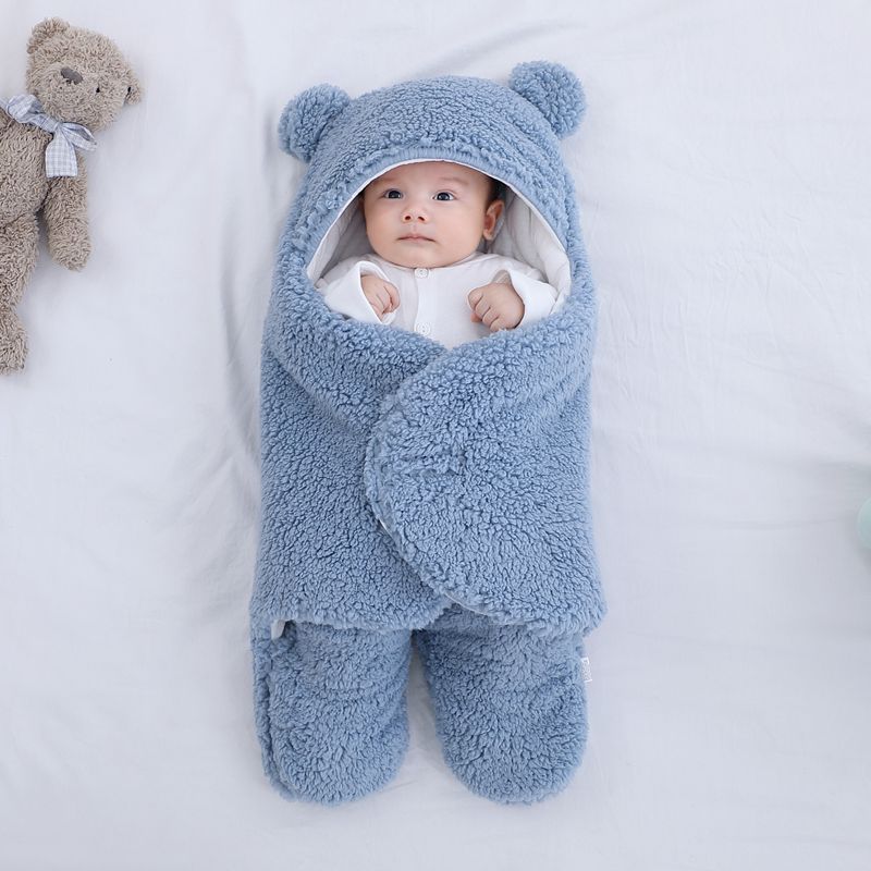Baby wrapped in a blue fluffy swaddle with a teddy bear on a white background