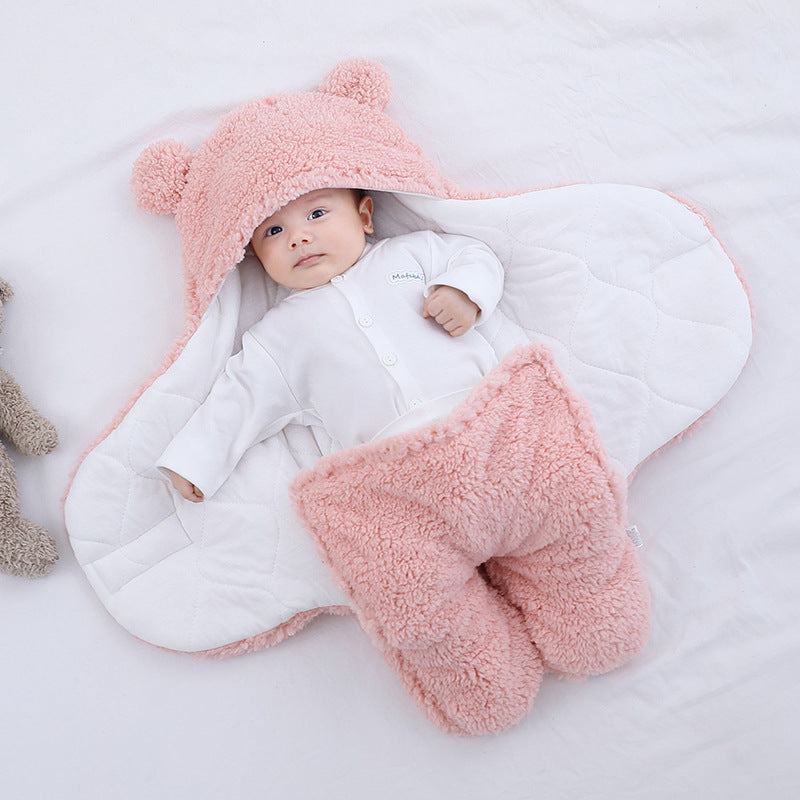 Baby wrapped in a pink and white fluffy blanket with a matching hat on a light background