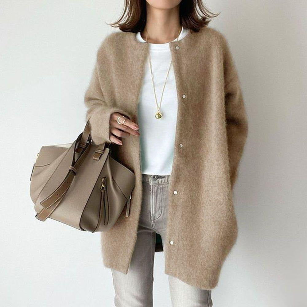 Person wearing a beige cardigan holding a matching handbag against a plain background