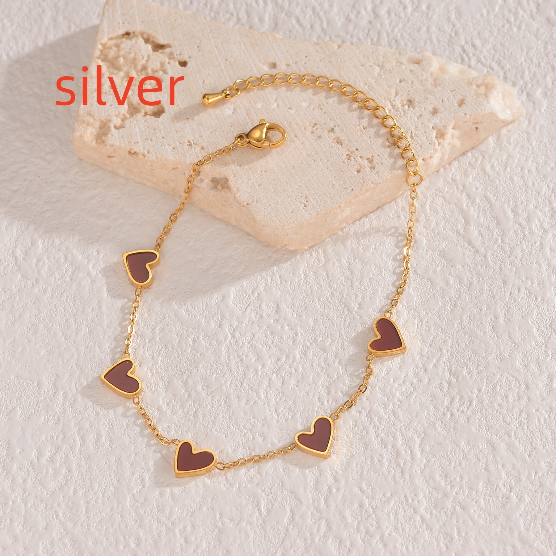 Gold bracelet with heart-shaped charms on a stone surface, labeled 'silver'.