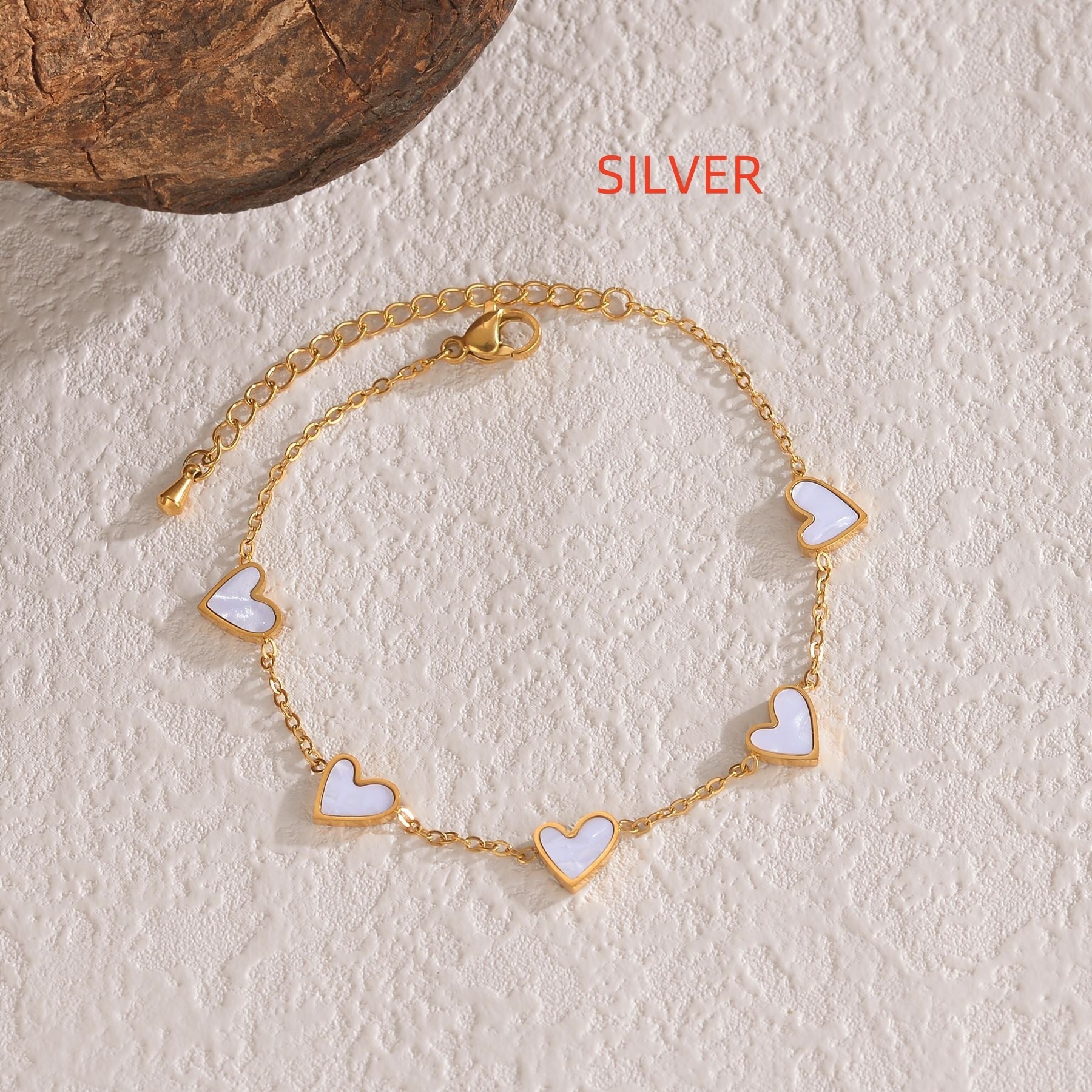 Gold bracelet with heart-shaped charms on a textured beige surface, labeled 'SILVER'.