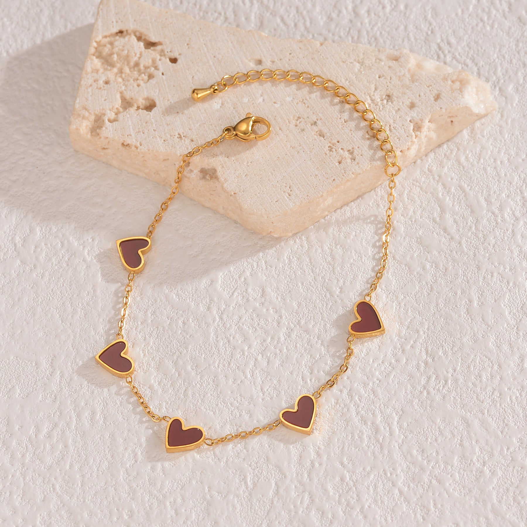 Gold bracelet with heart-shaped charms on a textured stone surface