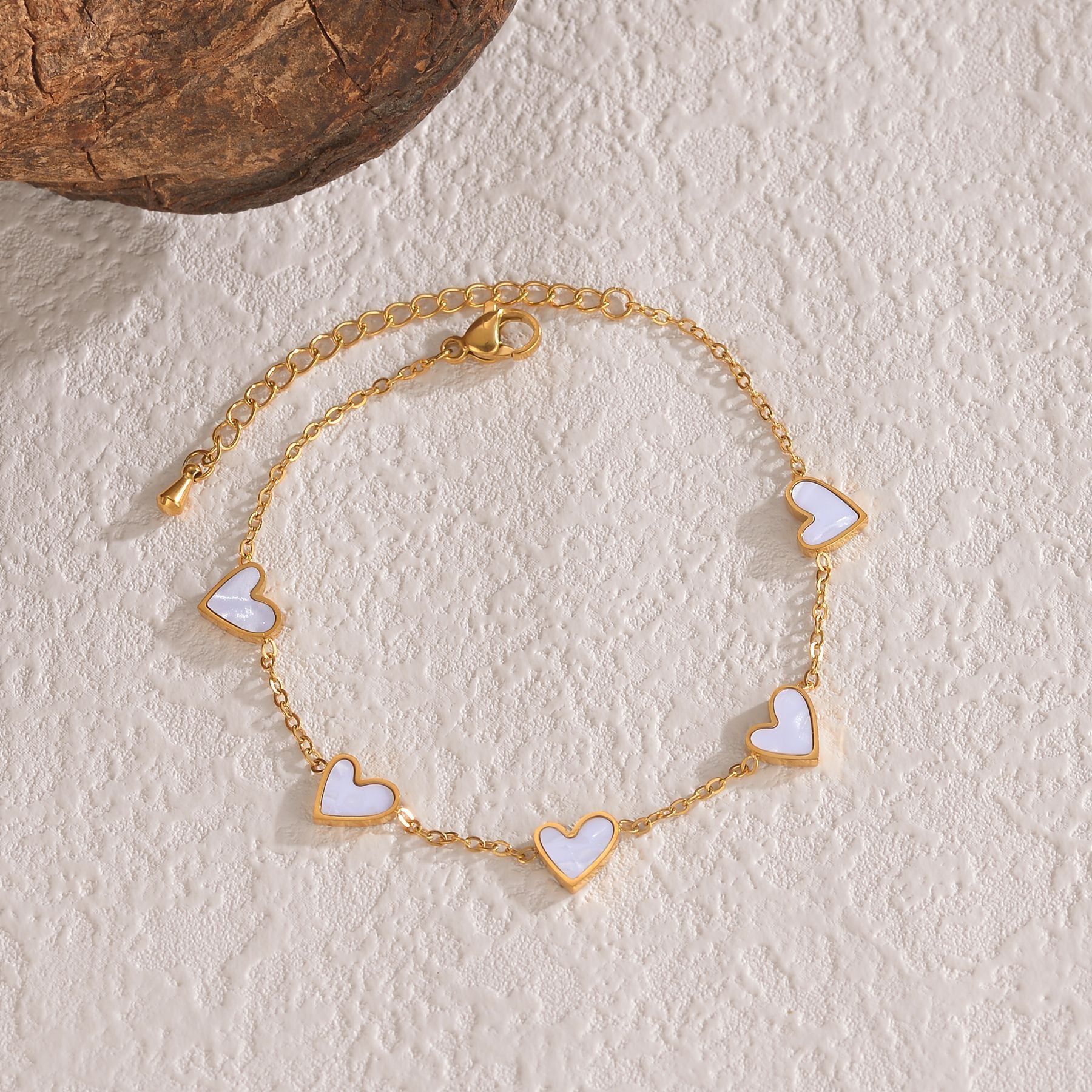 Gold bracelet with heart-shaped charms on a textured beige surface