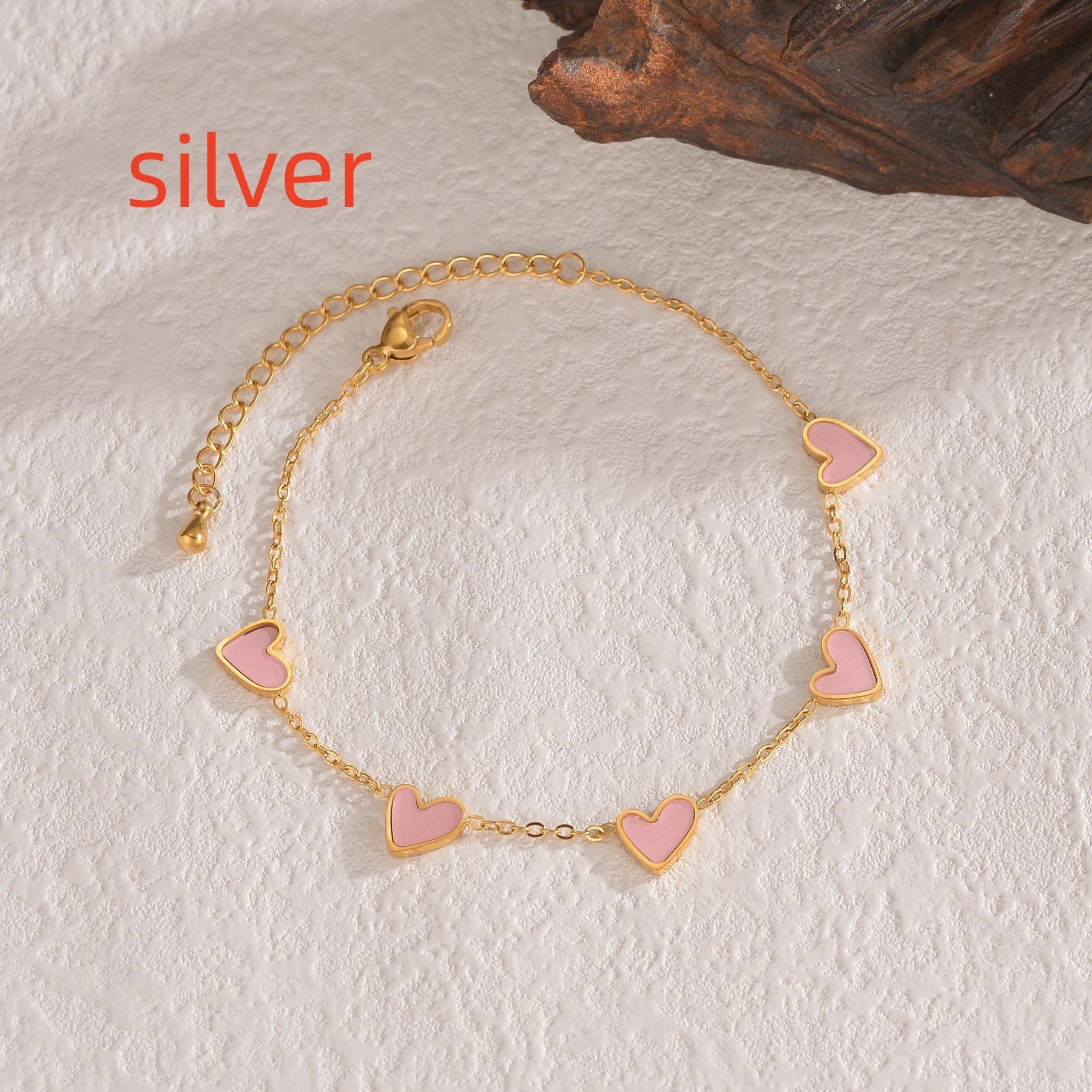 Gold bracelet with pink heart charms on a textured surface
