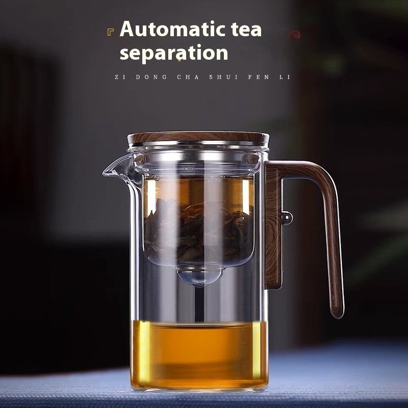 Clear glass teapot with wooden lid and handle, filled with tea, on a dark background.