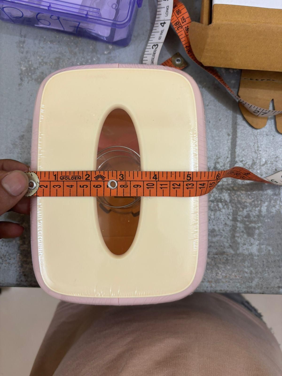 Measurement tape being used to measure a small box with a pink lid.