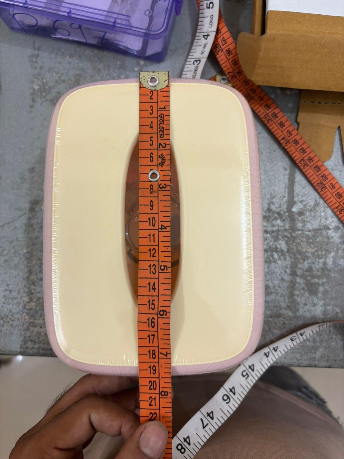 Rectangular beige cushion with a measuring tape on top, held by a hand.