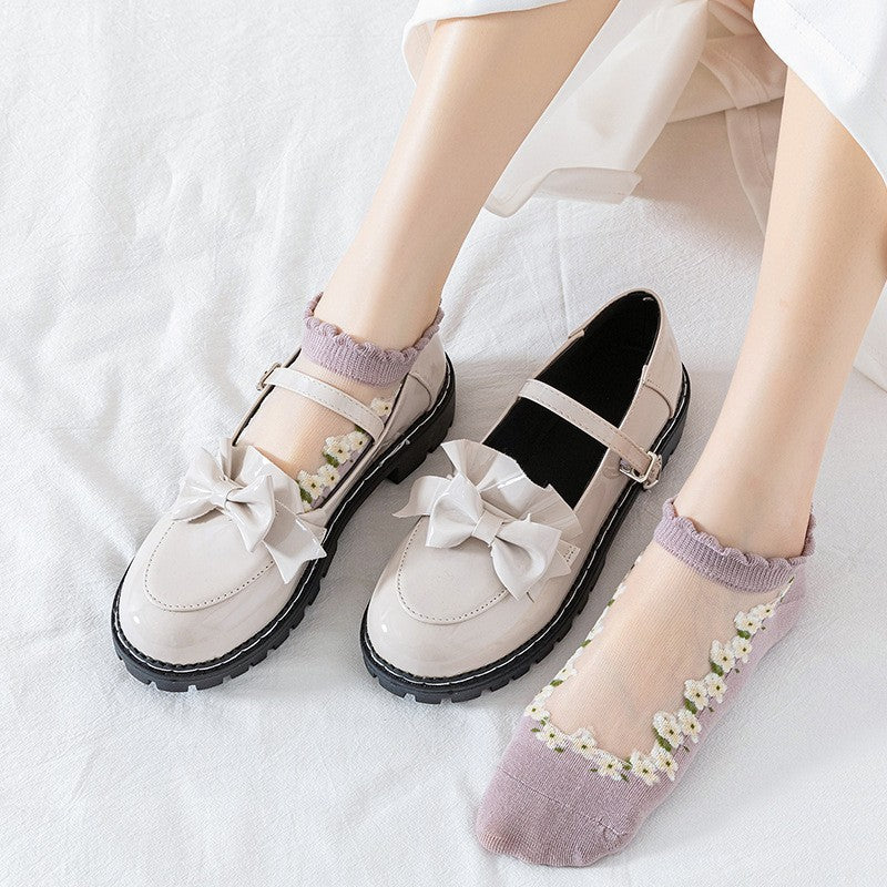 A pair of women's boat socks with a floral design in purple and white colors, worn with a pair of flat shoes.