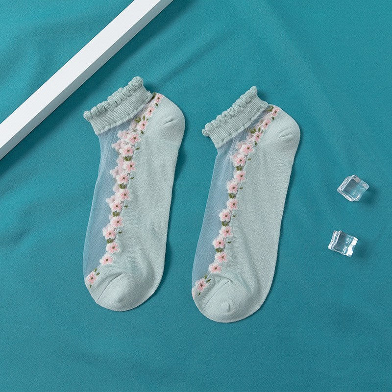 A pair of women's boat socks with a floral design in purple and white colors, worn with a pair of flat shoes.