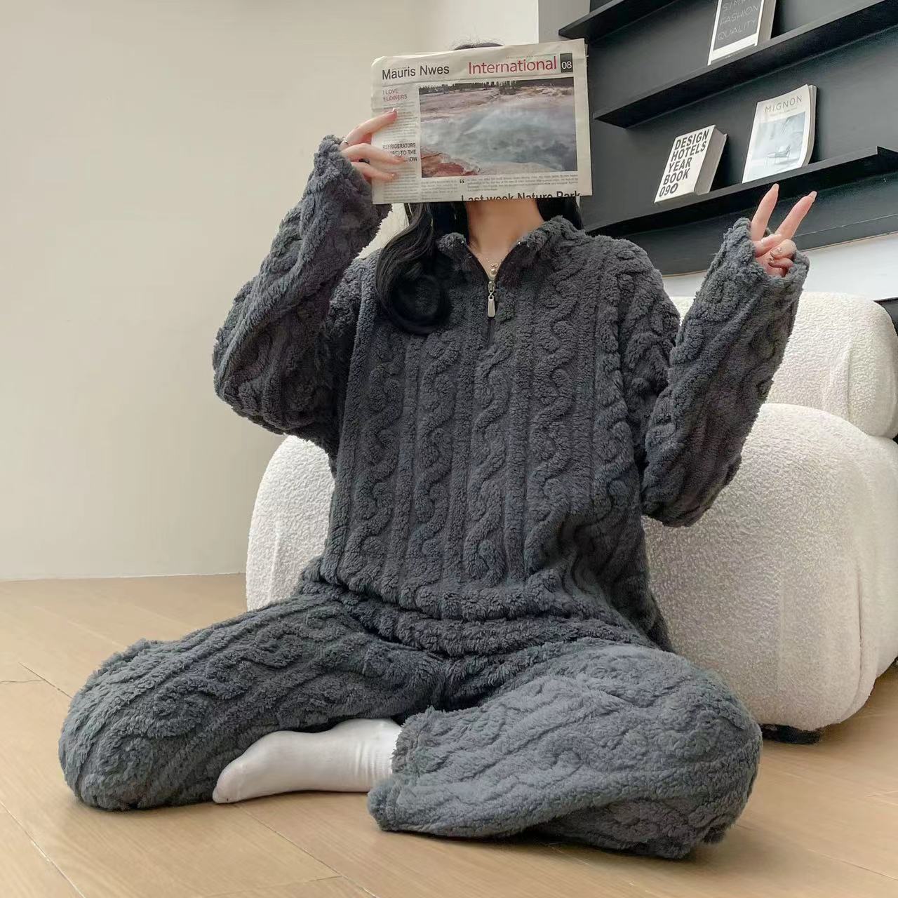 Person wearing a cozy gray cable knit onesie sitting on the floor with a newspaper.