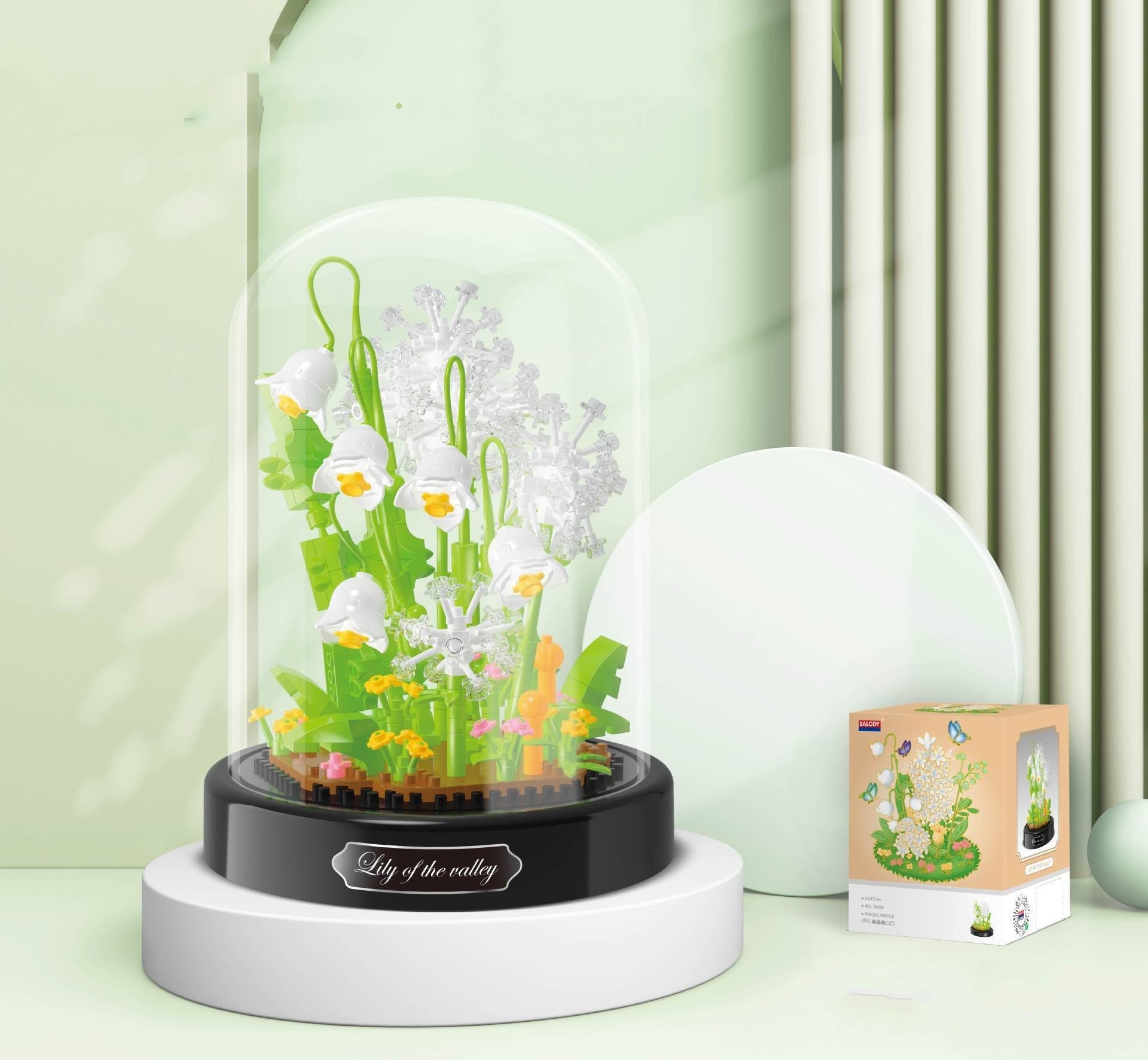 Decorative plant display with a clear dome on a white surface, featuring 'Lily of the valley' text.