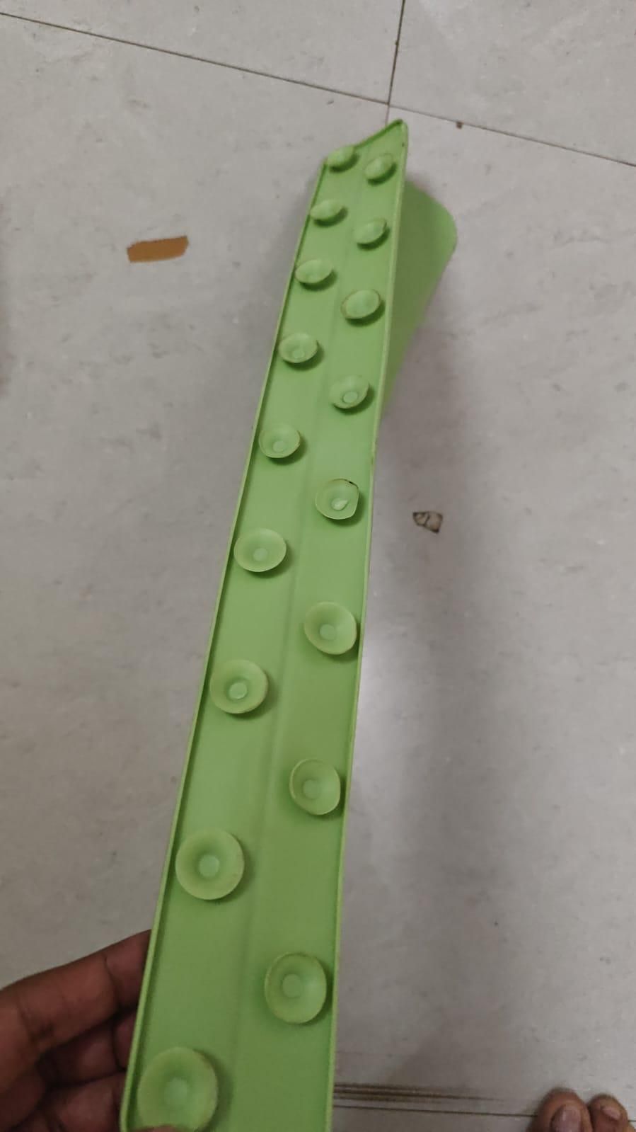 Green plastic block with round indentations on a light gray floor.