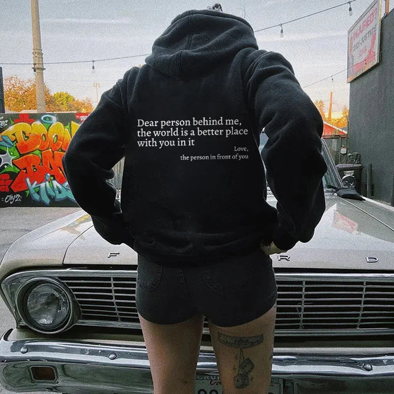 Person wearing a black hoodie with a quote on the back, standing in front of a classic car.