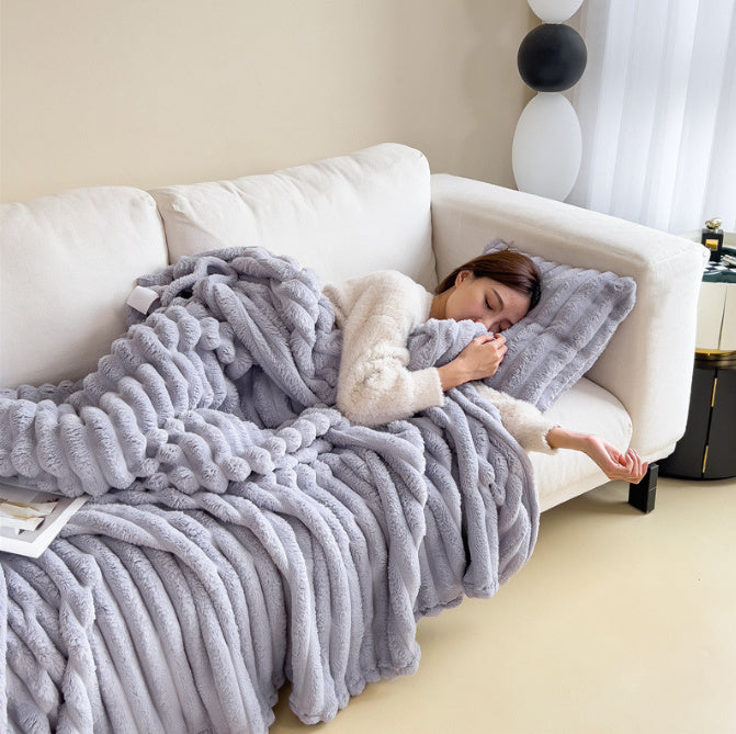 Woman lying on a white couch under a gray fluffy blanket in a cozy living room.