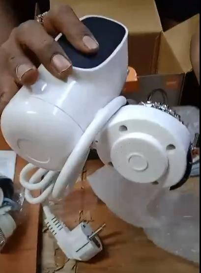 Hand holding a white electronic device with a black top on a wooden surface.