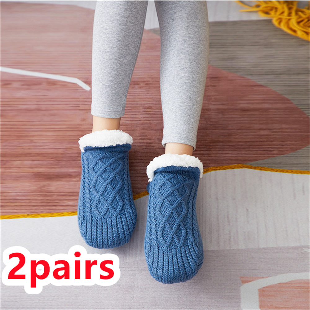 Blue knitted slippers with white fur lining worn by a person on a wooden floor.