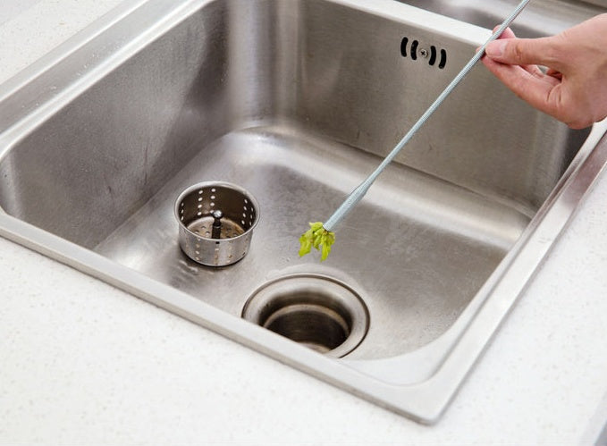 Person using a tool to clear a clogged drain in a stainless steel kitchen sink.